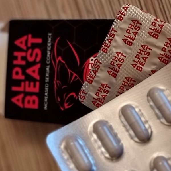 Dos blísteres plateados de Alpha Beast, uno vuelto con el nombre en rojo, ante la caja negra, sobre madera