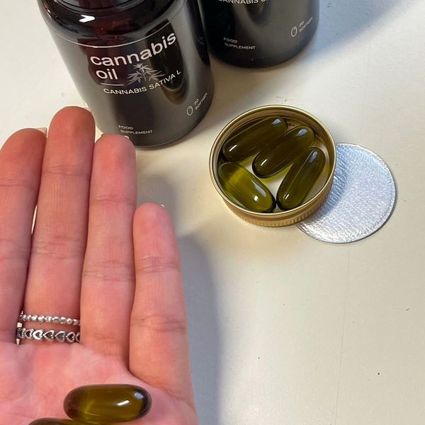 Perlas verdes de Cannabis Oil en la palma de la mano, junto al tarro abierto