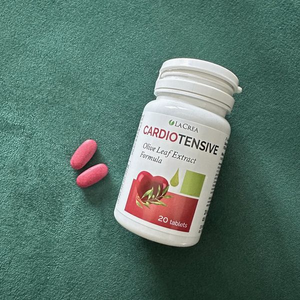 Bote de Cardiotensive con dos comprimidos rojos, sobre un tapete verde