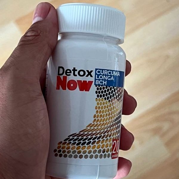 Bote blanco de Detox Now, Curcuma longa 8CH, con un dibujo de panal en tonos ocres, sujeto en una mano