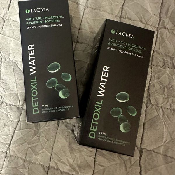Dos cajas negras de Detoxil Water, de 50 ml, con burbujas verdes dibujadas, sobre una colcha gris