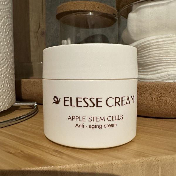 Tarro blanco mate de Elesse Cream, con letras marrones, en una balda de madera junto a discos de algodón