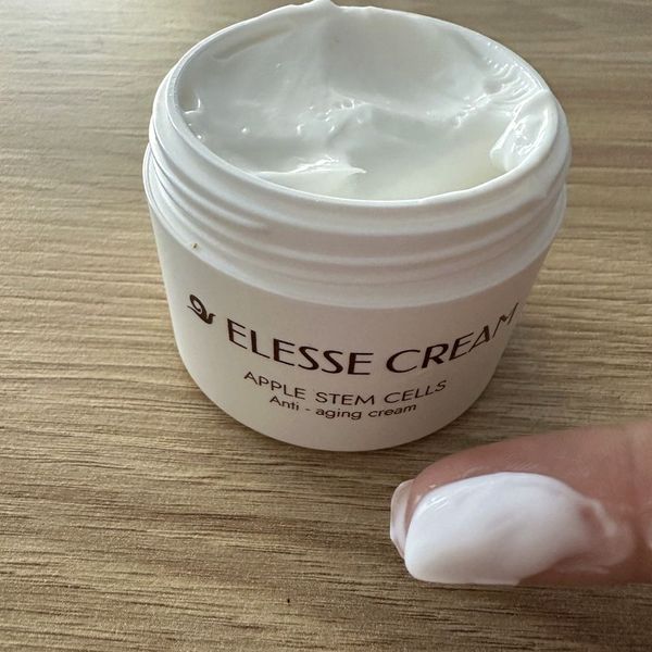Tarro de Elesse Cream abierto, con crema en la yema de un dedo