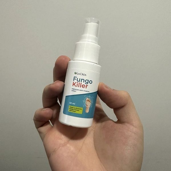 Frasco blanco de Fungo Killer con pulverizador, de 50 ml, sujeto en la palma de una mano ante una pared clara