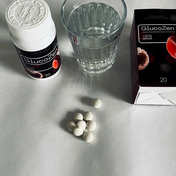 Comprimidos blancos de GlucoZen junto al bote, un vaso de agua y la caja