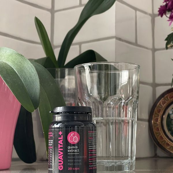 Bote negro de Guavital+ al lado de un vaso, con plantas al fondo