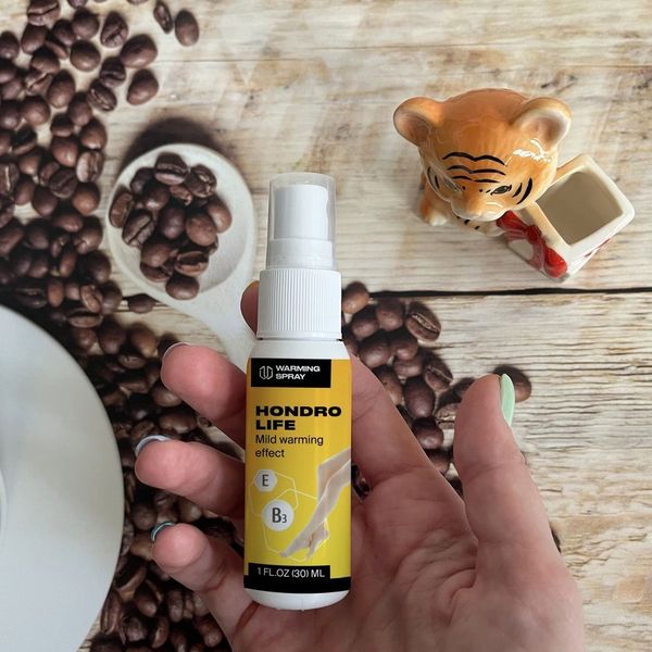 El frasco pulverizador blanco y amarillo de Hondrolife en una mano, sobre una mesa con granos de café