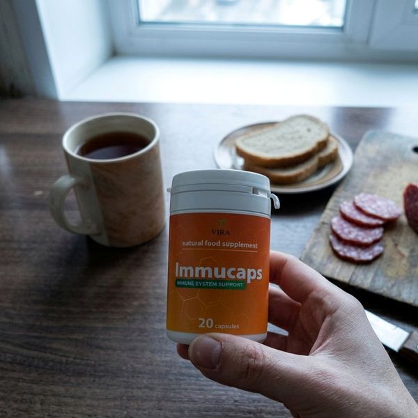 Mano que sostiene el bote de Immucaps junto a un desayuno