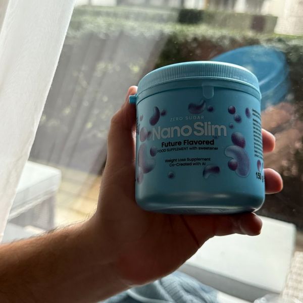 Mano que sostiene junto a una ventana el bote azul celeste de Nano Slim, de 150 g, con burbujas moradas