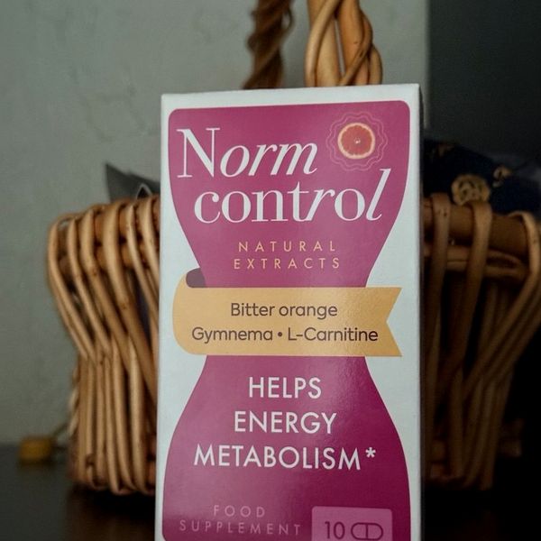 Caja blanca y fucsia de NormControl, 10 cápsulas, con reloj de arena y cítrico, ante una cesta de mimbre