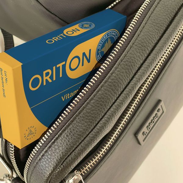 Caja azul marino y amarilla de Oriton asomando de un bolso de piel gris con la cremallera abierta