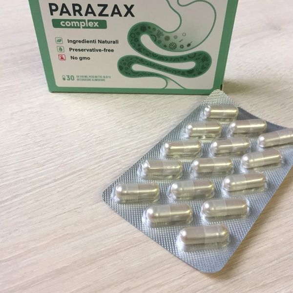 Caja verde y blanca de Parazax Complex detrás de un blíster de cápsulas nacaradas, sobre una mesa clara