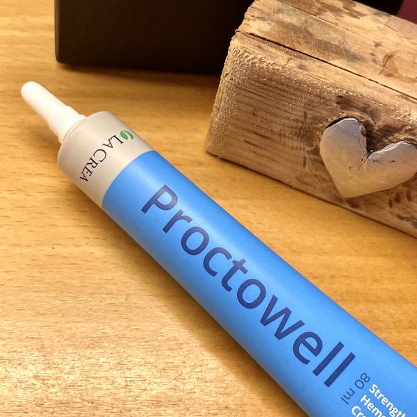 Primer plano del tubo azul de Proctowell, de 80 ml y con cánula larga, tumbado sobre una mesa de madera