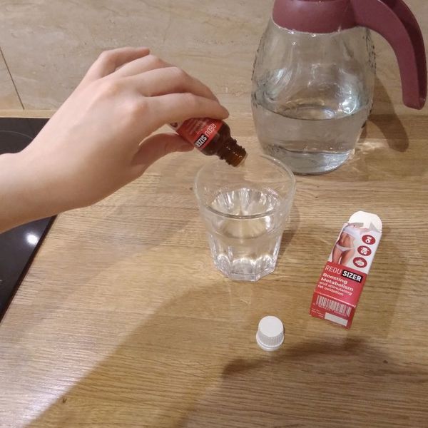 Gotas de Redusizer cayendo en un vaso de agua, con la caja al lado