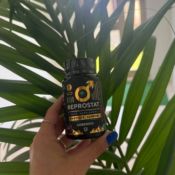 Mano que sostiene el bote de Reprostat delante de unas hojas de palmera