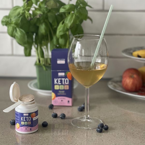 Slymsy Keto Drink en bote blanco con el cacito lleno, su caja morada y una copa con la bebida y una pajita
