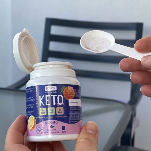 Bote de Slymsy Keto Drink abierto con el cacito de polvo en la mano