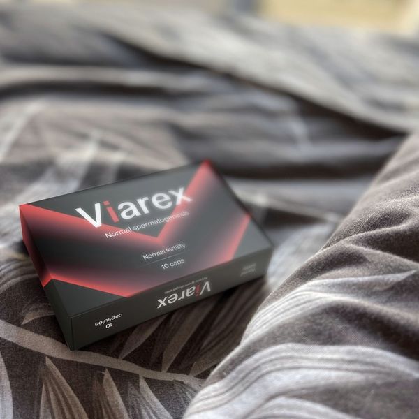 Caja negra de Viarex con una V roja luminosa, 10 cápsulas, apoyada sobre una sábana gris estampada
